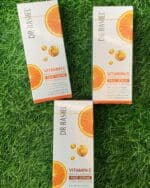 Three boxes of Dr Rashel Vitamin C Face Serum placed on green grass, showcasing brightening and anti-aging skincare with hyaluronic acid