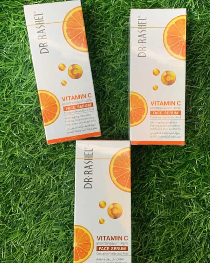 Three boxes of Dr Rashel Vitamin C Face Serum placed on green grass, showcasing brightening and anti-aging skincare with hyaluronic acid