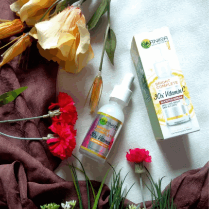 Garnier Bright Complete 30x Vitamin C Booster Serum bottle with box placed beside flowers, 30ml