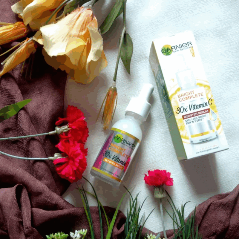 Garnier Bright Complete 30x Vitamin C Booster Serum bottle with box placed beside flowers, 30ml
