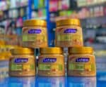 Five jars of La Fresh Gold Scrub 500ml with gold caps stacked on a reflective blue surface in a store display