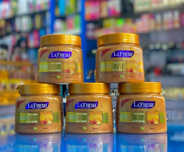 Five jars of La Fresh Gold Scrub 500ml with gold caps stacked on a reflective blue surface in a store display