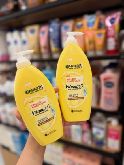 Two yellow bottles of Garnier Bright Complete Vitamin C Body Serum Lotion held in hand inside a store
