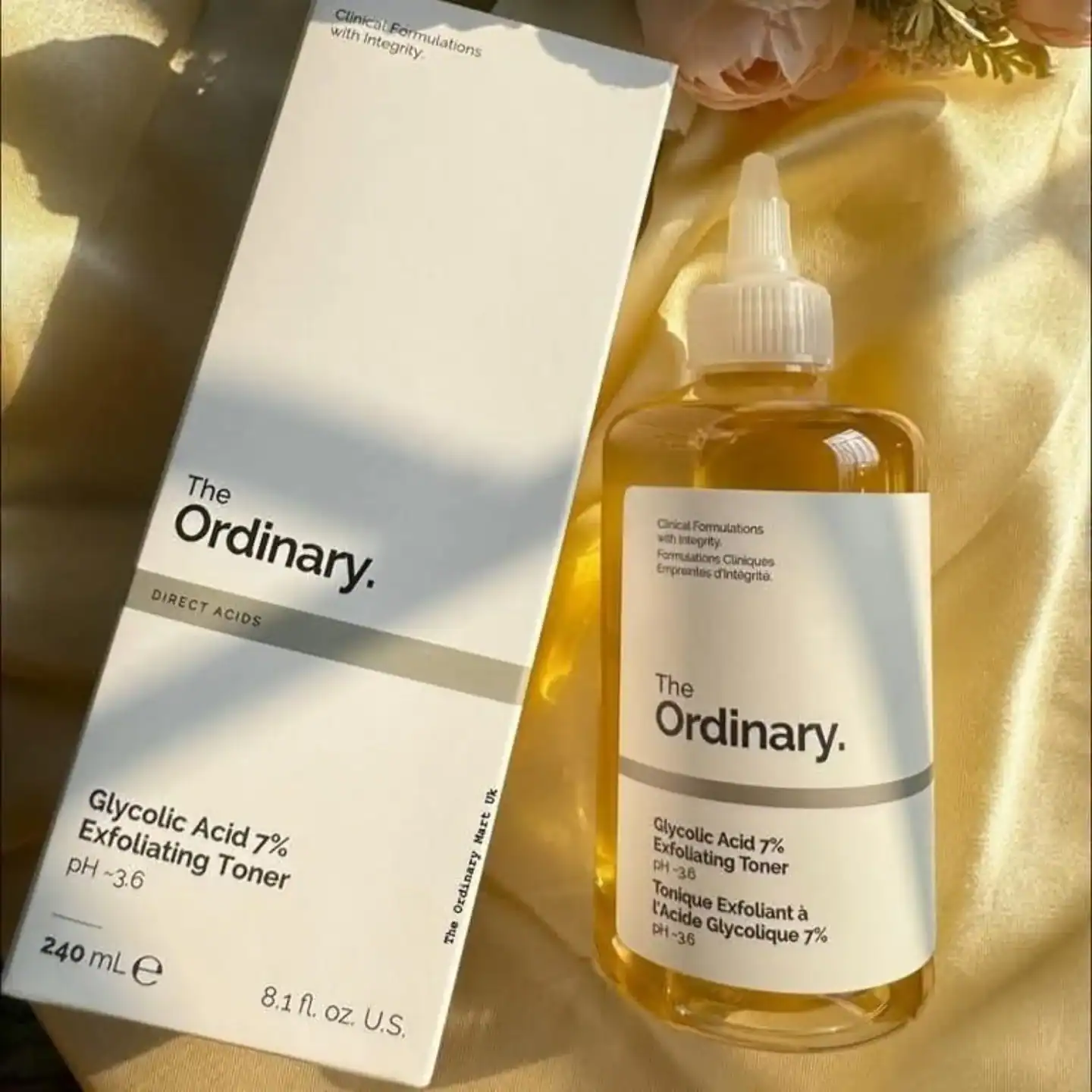 The Ordinary Glycolic Acid 7% Exfoliating Toner 240ml bottle with white label and box, placed on a gold satin background
