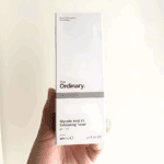 Hand holding The Ordinary Glycolic Acid 7% Exfoliating Toner 100ml box with minimalistic white packaging.