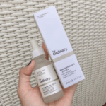 Hand holding The Ordinary Niacinamide 10% + Zinc 1% serum bottle and its box, 30ml packaging, high-strength vitamin and mineral formula for blemishes, oil control, and clearer skin.