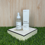 The Ordinary Niacinamide 10% + Zinc 1% serum 30ml placed beside its box on a decorative surface with wooden background and green grass, high-strength vitamin and mineral formula for blemish-prone skin and oil regulation.