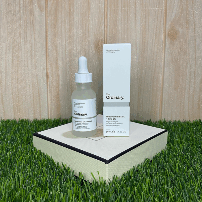 The Ordinary Niacinamide 10% + Zinc 1% serum 30ml placed beside its box on a decorative surface with wooden background and green grass, high-strength vitamin and mineral formula for blemish-prone skin and oil regulation.