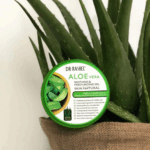 Dr Rashel Aloe Vera Soothing & Moisturizing Gel tub placed in front of a fresh aloe vera plant in a jute pot. Green lid packaging highlights hydration, glowing skin, cooling effect, and multipurpose skincare benefits.