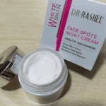 Open jar of Dr Rashel White Skin Fade Spots Night Cream with glossy silver lid, showing the creamy texture inside, placed beside its box highlighting Arbutin and Niacinamide for even skin tone and dark spot reduction.