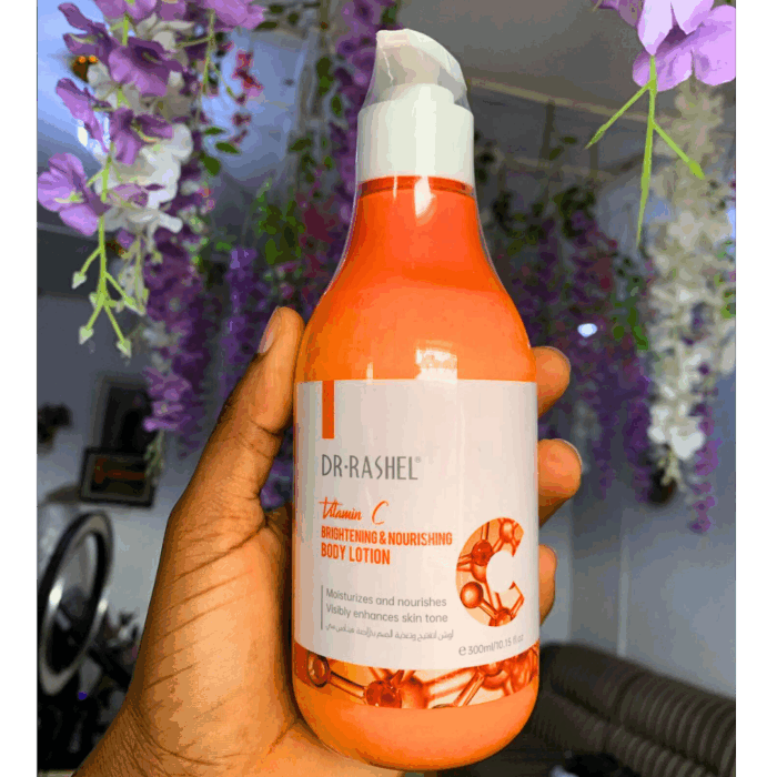 Hand holding Dr Rashel Vitamin C Brightening & Nourishing Body Lotion 300ml bottle with floral background.