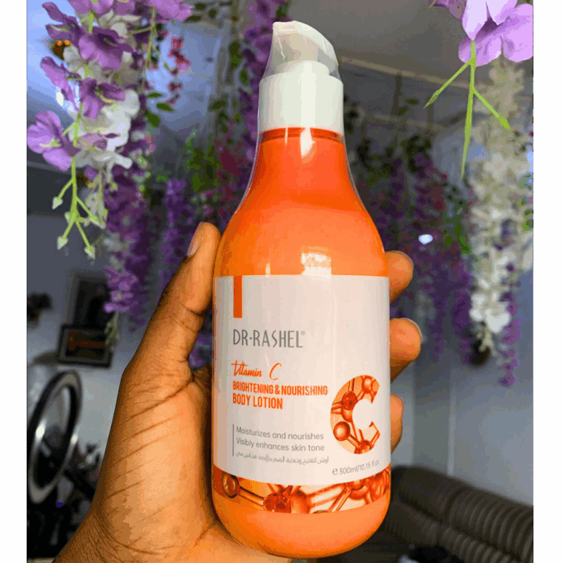 Hand holding Dr Rashel Vitamin C Brightening & Nourishing Body Lotion 300ml bottle with floral background.