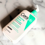 CeraVe Foaming Facial Cleanser bottle placed on marble surface with cleanser texture nearby.
