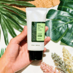 Hand holding COSRX Aloe Soothing Sun Cream SPF 50+ PA+++ against green leaves background.