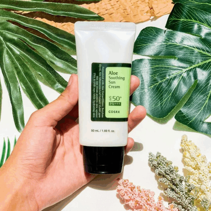 Hand holding COSRX Aloe Soothing Sun Cream SPF 50+ PA+++ against green leaves background.