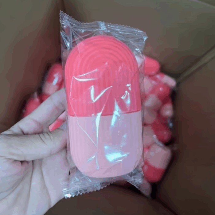 Hand holding a sealed pink capsule-shaped ice roller mold in transparent packaging.