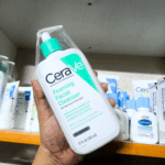 Hand holding CeraVe Foaming Facial Cleanser 355ml in a store shelf with other skincare products.
