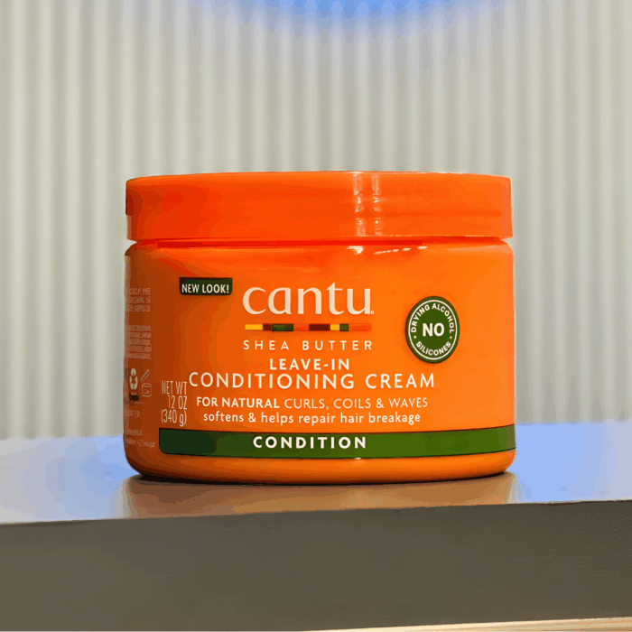 Cantu Shea Butter Leave-In Conditioning Cream jar placed on a table, designed to condition, soften, and repair breakage for natural curls, coils, and waves.