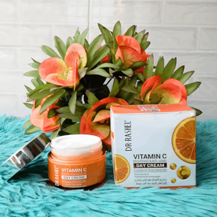 An open jar and packaging box of Dr Rashel Vitamin C Brightening & Anti-Aging Day Cream placed on a turquoise surface with orange flowers in the background, highlighting its niacinamide and antioxidant formula.