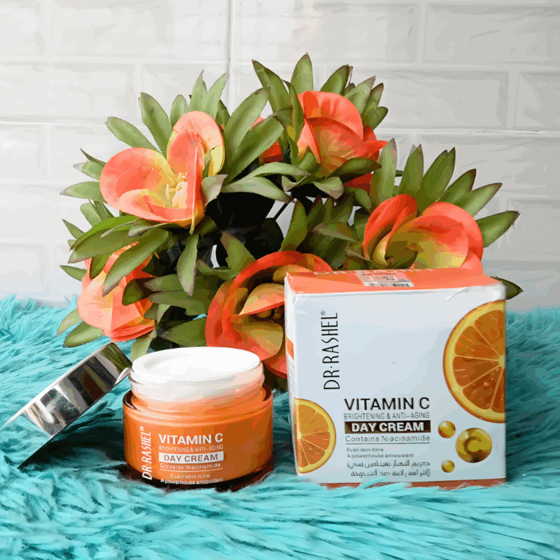An open jar and packaging box of Dr Rashel Vitamin C Brightening & Anti-Aging Day Cream placed on a turquoise surface with orange flowers in the background, highlighting its niacinamide and antioxidant formula.