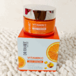A jar of Dr Rashel Vitamin C Brightening & Anti-Aging Day Cream placed on top of its box, featuring orange and silver packaging that highlights niacinamide and antioxidant benefits for glowing skin.