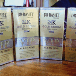Multiple boxes of Dr Rashel 24K Gold Serum VIP All In One lined up on a wooden surface, showing the gold packaging with “24K Pure Gold 99.9%” and product benefits.