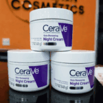 Three jars of CeraVe Skin Renewing Night Cream stacked together on a glossy surface with an orange cosmetics-store background.
