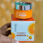 A person holding Dr Rashel Vitamin C Brightening & Anti-Aging Day Cream on top of its box, showing the vibrant orange packaging enriched with niacinamide and vitamin C for glowing, even-toned skin.