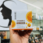 A hand holding Dr Rashel Vitamin C Brightening & Anti-Aging Day Cream box, featuring orange slice graphics and niacinamide formula for radiant, even-toned skin.