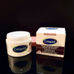 An open jar of Cetaphil Healthy Radiance Brightening Cream 50g with its box beside it on a glossy black surface, showing the creamy texture and product packaging.