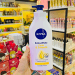 Person holding a Nivea Extra White Firm & Smooth Body Lotion bottle inside a brightly lit store with beauty products in the background, highlighting Q10 and Vitamin C benefits.