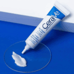 CeraVe Eye Repair Cream tube on a blue background with a small amount of cream shown, illustrating its smooth, hydrating texture for brightening and soothing the under-eye area.