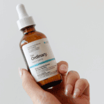 Hand holding The Ordinary Multi-Peptide Serum for Hair Density bottle with dropper cap. The amber bottle features a white and blue label promoting thicker, fuller, and healthier-looking hair through concentrated peptide technology.