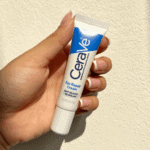 Person holding a CeraVe Eye Repair Cream 14.2g tube under natural sunlight against a white background, showcasing its compact design and blue-and-white packaging.