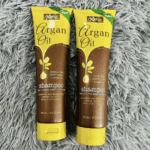 Two tubes of XHC Argan Oil Shampoo placed on a soft grey rug. The green and brown packaging highlights its hydrating, nourishing, and cleansing benefits with Moroccan argan oil extracts, SLS-free and paraben-free formula.