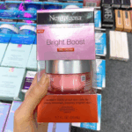 Person holding a boxed jar of Neutrogena Bright Boost Gel Cream (50ml) with pink and silver packaging, designed to brighten dull skin and enhance glow using Accelerated Brightening Complex.