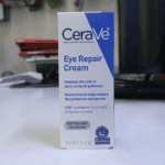 Close-up of a CeraVe Eye Repair Cream 14.2g box on a white table, highlighting product claims about reducing dark circles and puffiness with ceramides and hyaluronic acid.