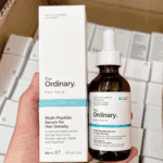 Hand holding The Ordinary Multi-Peptide Serum for Hair Density with its box. The 60ml amber bottle features a white dropper cap and label highlighting the serum’s benefits for thicker, fuller, and healthier-looking hair.