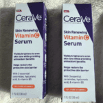 Two boxes of CeraVe Skin Renewing Vitamin C Serum placed on a soft beige surface. Packaging highlights its 10% Pure Vitamin C, ceramides, hyaluronic acid, and vitamin B5 that brighten and restore skin tone.