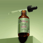 Open Mielle Rosemary Mint hair oil bottle with dropper showing lightweight oil texture against green background.