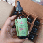 Mielle Rosemary Mint hair strengthening oil bottle held above open shipping carton with multiple bottles inside.