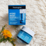 Neutrogena Hydro Boost Water Gel 50ml with Hyaluronic Acid placed beside its blue retail box on a soft cream surface with a yellow flower. The product packaging highlights 72-hour hydration for supple, dewy skin and is ideal for normal to combination skin.