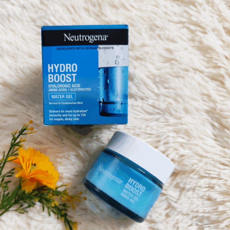 Neutrogena Hydro Boost Water Gel 50ml with Hyaluronic Acid placed beside its blue retail box on a soft cream surface with a yellow flower. The product packaging highlights 72-hour hydration for supple, dewy skin and is ideal for normal to combination skin.