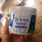 Hand holding St. Ives Renewing Moisturizer Collagen & Elastin tub showing the front label under indoor lighting.