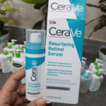Hand holding CeraVe Resurfacing Retinol Serum bottle beside box packaging on store counter with skincare products