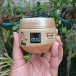 Hand holding Gluta White glutathione collagen whitening cream jar in natural outdoor setting