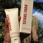 Hand holding Seoul 1988 snail mucin rice cream tube and box outdoors in sunlight