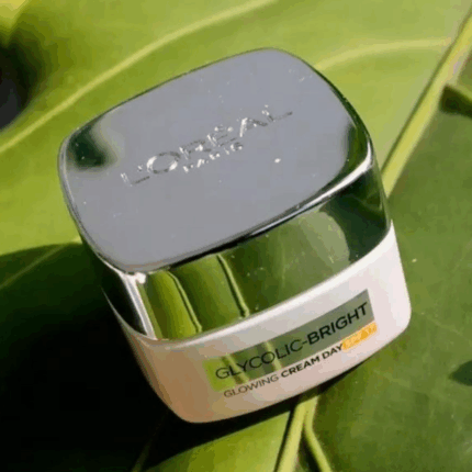 L’Oréal Glycolic Bright Glowing Day Cream SPF 17 jar placed on green leaf background
