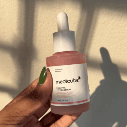 Hand holding Medicube PDRN Pink Peptide Serum showing pink serum texture in bottle