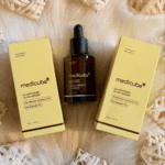 Medicube Glutathione Glow Serum bottle placed between two product boxes on soft surface